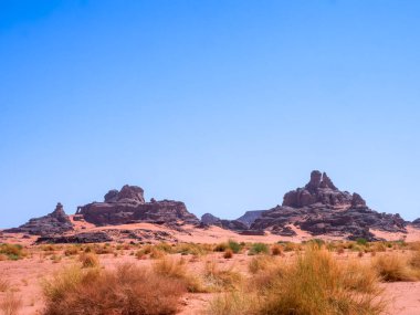 Sahra Çölü 'ndeki Kızıl Tadrart' ın kaya oluşumları ve altın tepecikleri. Berrak bir gökyüzünün altında çarpıcı bir doğal manzara. Sahra Çölü, Cezayir 'de gün doğumunda kum tepeleri ve kaya oluşumlarıyla Kızıl Tadrart' ın manzarası.