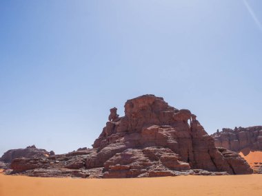 Sahra Çölü 'ndeki Kızıl Tadrart' ın kaya oluşumları ve altın tepecikleri. Berrak bir gökyüzünün altında çarpıcı bir doğal manzara. Sahra Çölü, Cezayir 'de gün doğumunda kum tepeleri ve kaya oluşumlarıyla Kızıl Tadrart' ın manzarası.