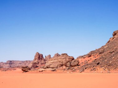 Sahra Çölü 'ndeki Kızıl Tadrart' ın kaya oluşumları ve altın tepecikleri. Berrak bir gökyüzünün altında çarpıcı bir doğal manzara. Sahra Çölü, Cezayir 'de gün doğumunda kum tepeleri ve kaya oluşumlarıyla Kızıl Tadrart' ın manzarası.