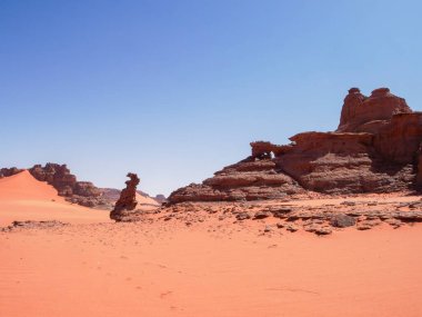 Sahra Çölü 'ndeki Kızıl Tadrart' ın kaya oluşumları ve altın tepecikleri. Berrak bir gökyüzünün altında çarpıcı bir doğal manzara. Sahra Çölü, Cezayir 'de gün doğumunda kum tepeleri ve kaya oluşumlarıyla Kızıl Tadrart' ın manzarası.