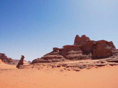 Sahra Çölü 'ndeki Kızıl Tadrart' ın kaya oluşumları ve altın tepecikleri. Berrak bir gökyüzünün altında çarpıcı bir doğal manzara. Sahra Çölü, Cezayir 'de gün doğumunda kum tepeleri ve kaya oluşumlarıyla Kızıl Tadrart' ın manzarası.