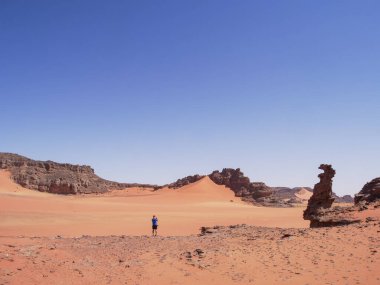 Sahra Çölü 'ndeki Kızıl Tadrart' ın kaya oluşumları ve altın tepecikleri. Berrak bir gökyüzünün altında çarpıcı bir doğal manzara. Sahra Çölü, Cezayir 'de gün doğumunda kum tepeleri ve kaya oluşumlarıyla Kızıl Tadrart' ın manzarası.