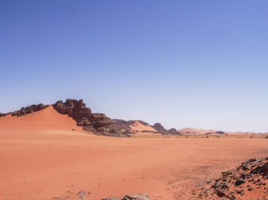 Sahra Çölü 'ndeki Kızıl Tadrart' ın kaya oluşumları ve altın tepecikleri. Berrak bir gökyüzünün altında çarpıcı bir doğal manzara. Sahra Çölü, Cezayir 'de gün doğumunda kum tepeleri ve kaya oluşumlarıyla Kızıl Tadrart' ın manzarası.