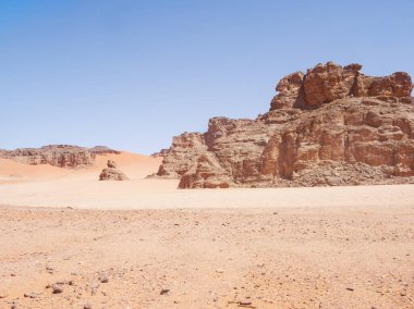 Sahra Çölü 'ndeki Kızıl Tadrart' ın kaya oluşumları ve altın tepecikleri. Berrak bir gökyüzünün altında çarpıcı bir doğal manzara. Sahra Çölü, Cezayir 'de gün doğumunda kum tepeleri ve kaya oluşumlarıyla Kızıl Tadrart' ın manzarası.