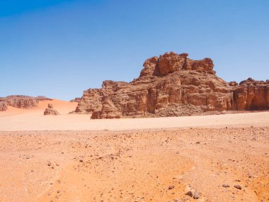 Sahra Çölü 'ndeki Kızıl Tadrart' ın kaya oluşumları ve altın tepecikleri. Berrak bir gökyüzünün altında çarpıcı bir doğal manzara. Sahra Çölü, Cezayir 'de gün doğumunda kum tepeleri ve kaya oluşumlarıyla Kızıl Tadrart' ın manzarası.