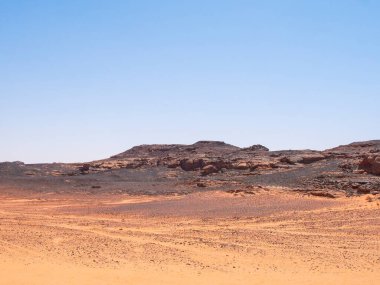 Sahra Çölü 'ndeki Kızıl Tadrart' ın kaya oluşumları ve altın tepecikleri. Berrak bir gökyüzünün altında çarpıcı bir doğal manzara. Sahra Çölü, Cezayir 'de gün doğumunda kum tepeleri ve kaya oluşumlarıyla Kızıl Tadrart' ın manzarası.