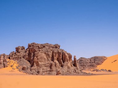 Kızıl Tadrart 'ın çöl manzarası. Mavi gökyüzünün altında kaya oluşumları ve altın kum. Cezayir Sahra 'sının doğal manzarası.
