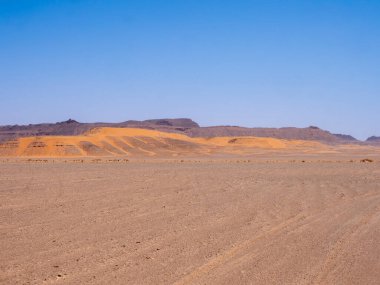 Kızıl Tadrart 'ın çöl manzarası. Mavi gökyüzünün altında kaya oluşumları ve altın kum. Cezayir Sahra 'sının doğal manzarası.