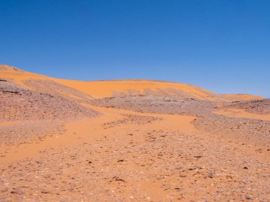 Kızıl Tadrart 'ın çöl manzarası. Mavi gökyüzünün altında kaya oluşumları ve altın kum. Cezayir Sahra 'sının doğal manzarası.