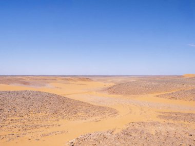 Kızıl Tadrart 'ın çöl manzarası. Mavi gökyüzünün altında kaya oluşumları ve altın kum. Cezayir Sahra 'sının doğal manzarası.