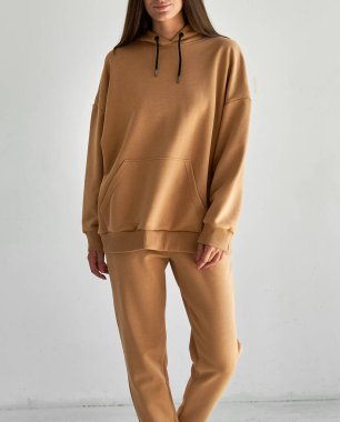 Uzun kollu kapüşonlu, bej bej bir kostüm.