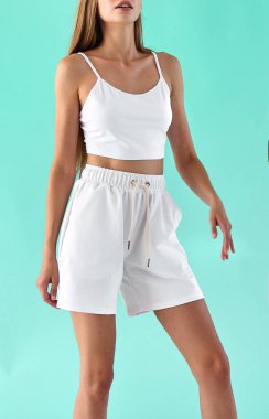 Genç kadın beyaz yaz kıyafetleri içinde duruyor. Beyaz kolsuz gömlek ve beyaz şort giyen bir kızın izole edilmiş portresi..