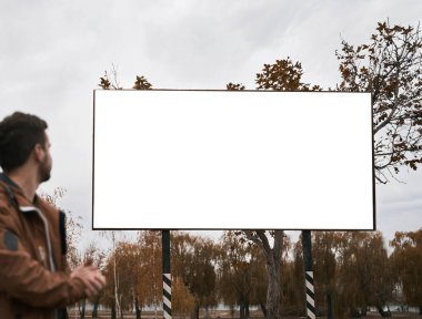 Sokakta duran ve reklam panosuna bakan bir adam. Erkek silueti ve boş poster. Açık hava yaşam tarzı reklam modeli