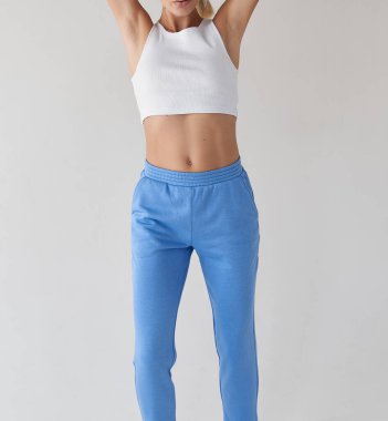 fit kız beyaz bluzlu açık mavi tekstil pantolon giyer. Genç bir kadın izole edilmiş günlük giysiler içinde duruyor.