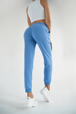 fit kız beyaz bluzlu açık mavi tekstil pantolon giyer. Genç bir kadın izole edilmiş günlük giysiler içinde duruyor.