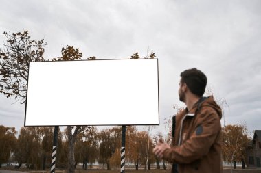 Sokakta duran ve reklam panosuna bakan bir adam. Erkek silueti ve boş poster. Açık hava yaşam tarzı reklam modeli