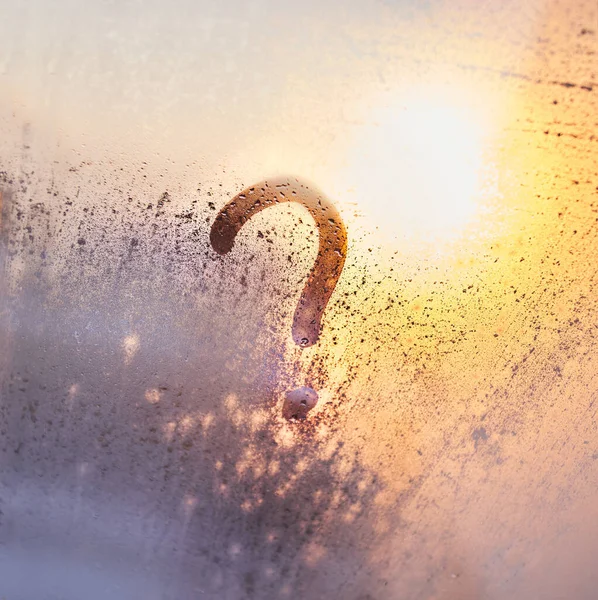 The question mark on the window with water drops on sunny background. Fogged window calligraphy