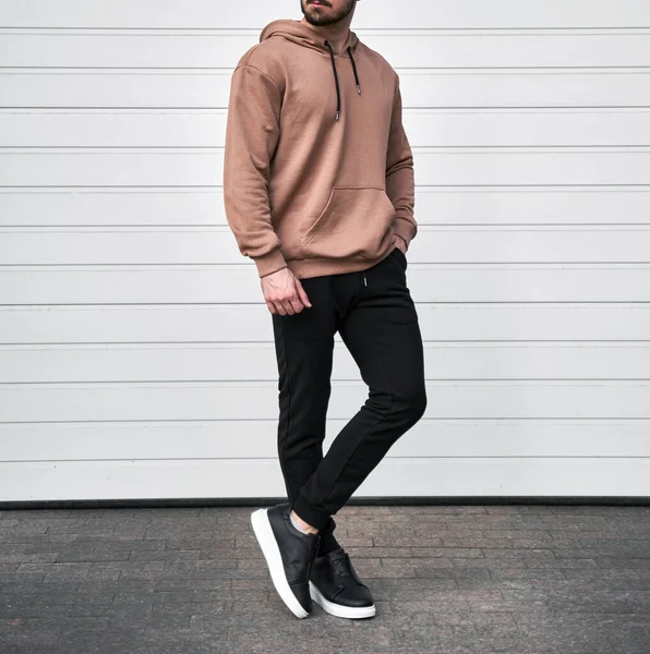 Man is standing in brown hoodie and dark pants. Man is wearing light suede stylish long sleeve sweater.