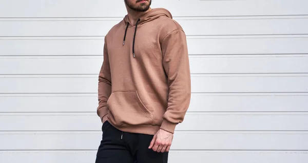 Man is standing in brown hoodie and dark pants. Man is wearing light suede stylish long sleeve sweater.