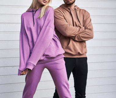 Sıradan sokak kıyafeti giyen bir çift. Kahverengi süet süveterli bir adam. Kadın pembe mor yün kapüşon ve pantolon giyiyor.