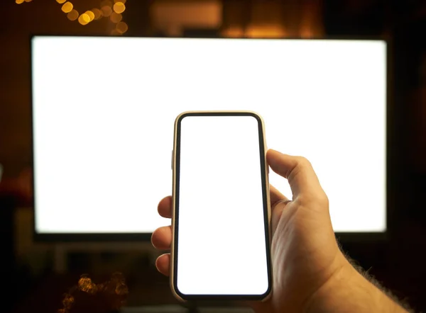 Photo of the white blank screen of the computer and hand holding cellphone. Digital web space concept