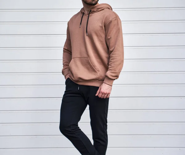 Man is standing in brown hoodie and dark pants. Man is wearing light suede stylish long sleeve sweater.