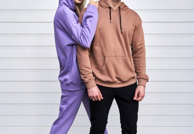 Sıradan sokak kıyafeti giyen bir çift. Kahverengi süet süveterli bir adam. Kadın pembe mor yün kapüşon ve pantolon giyiyor.