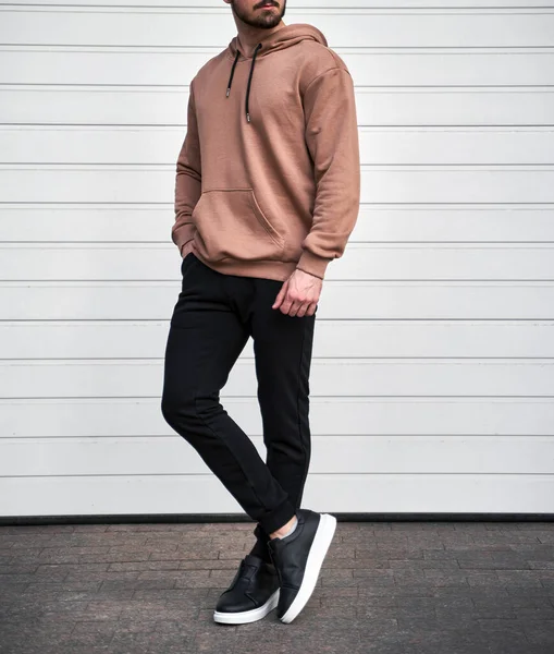 Man is standing in brown hoodie and dark pants. Man is wearing light suede stylish long sleeve sweater.