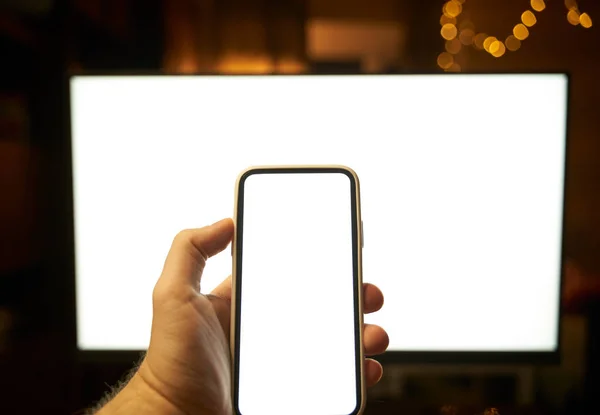 Photo of the white blank screen of the computer and hand holding cellphone. Digital web space concept