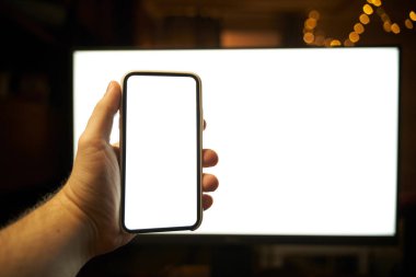 Arka planda bilgisayar monitörü olan modern akıllı telefonun el modeli. Boş ekran tasarım şablonu