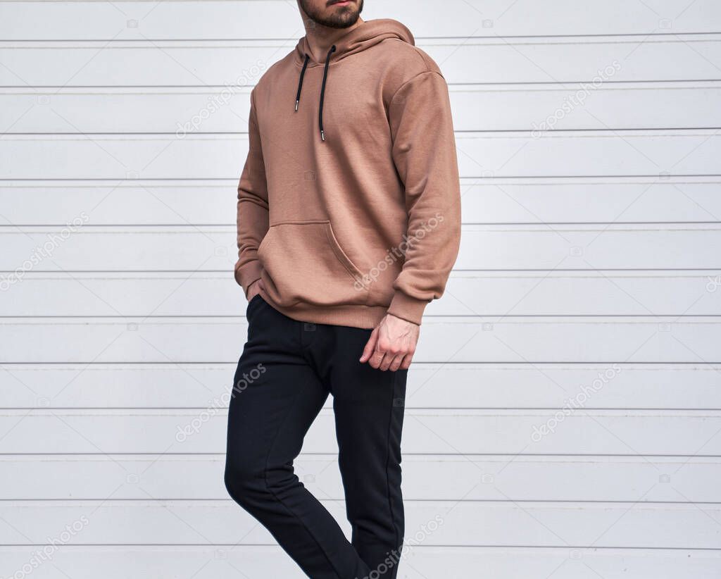 Man is standing in brown hoodie and dark pants. Man is wearing light suede stylish long sleeve sweater.
