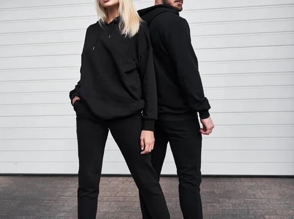 Woman and man wear black hoodie without a logo. No logo basic sportswear. Long sleeve sweatshirt mockup