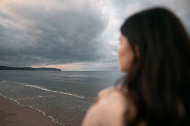 Yalnız kadın sahilde yürüyor. Akşamları deniz kenarında yürüyen esmer elbiseli bir kadın. Baharda deniz kenarında bir kız..