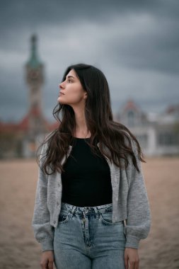Bulutlu bir akşamda kumsalda uzun siyah saçlı bir genç. Esmer kız soğuk bir akşamda deniz kenarında kıyafet giyer. Yalnız kadının izole edilmiş portresi..