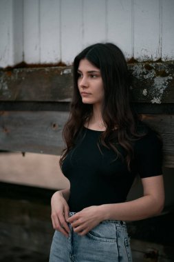 Kumsalda şehvetli ve muhteşem bir esmer. Sahilde sonbahar sezonu boyunca giyinik bir kadın. Siyah gömlek ve kot pantolon giyen kahverengi saçlı bir kızın portresi..