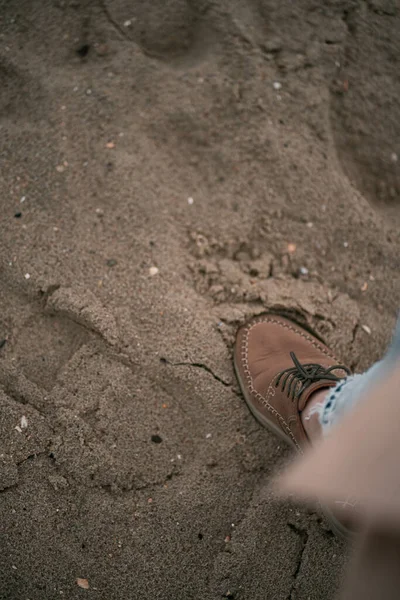 Girl wearing boots and jeans on the beach. Close up of human walking clothed on the sand beach during cold weather. Shoe on the beach sand. Fashionable and trendy  footwear.