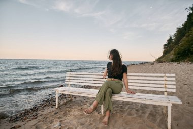 Çekici esmer kumsalda oturuyor. Deniz kenarındaki güzel yerde dinginlik kavramı