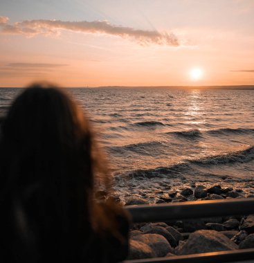 Yalnız bir kadının bulanık silueti denizin üzerinde gün batımını seyrediyor..