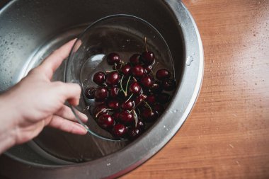 Akan suyun altında tatlı kirazları yıkıyorum. Olgun koyu kırmızı kirazları duruluyorum. Yaz konsepti boyunca vitamin dolu sağlıklı ve lezzetli yiyecekler..
