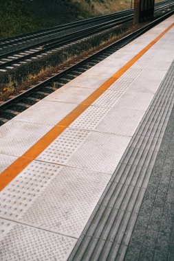 Tren platformunun zemininde şablon var. Sarı güdüm tamponları ve görme engelli insanlar için çizgileri olan tren istasyonu. Çelik raylar.