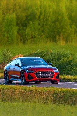 Kırsal yolda kırmızı spor araba sürüyor.