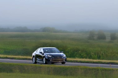 Açık yolda parlak yeni bir otomobil sürüyor.