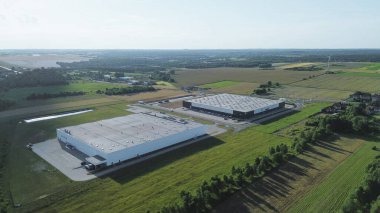 Tarlalar ve ağaçlarla çevrili iki büyük depo.