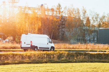 Kırsal yolda beyaz minibüs sürüyor.