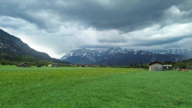 Bulutların altındaki çayırlarda ahşap barakalar.