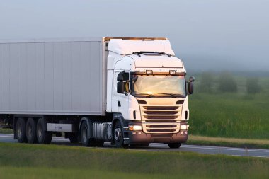 Kırsal yolda beyaz kargo kamyonu sürüyor.