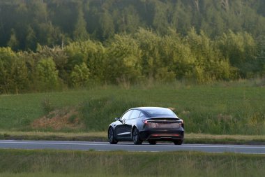 Melez araç manzaralı bir kırsal yolda ilerliyor.