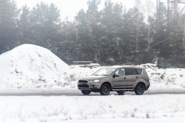 Kış boyunca karlı yol kenarında giden SUV.