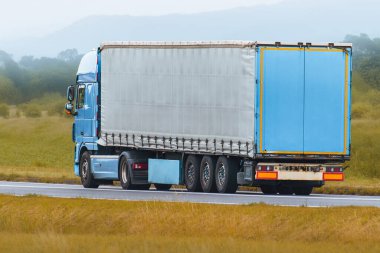 Kırsal yolda beyaz kargo kamyonu sürüyor.