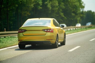 Orman yolunda giden sarı sedan.